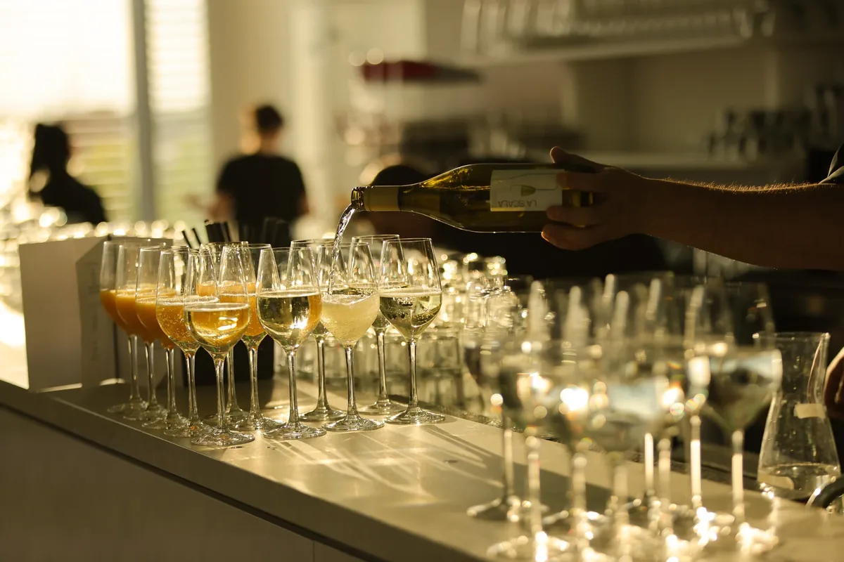 Weißwein wird an der Bar in eine Reihe Gläser eingeschenkt – Getränkefotografie beim Event