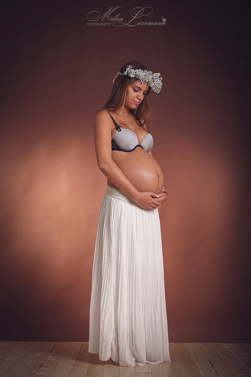 Schwangere im weißen Kleid hält ihren Babybauch – Babybauchshooting Berlin